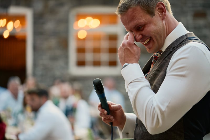 a male member of the wedding party holding a mic and wiping a tear from his eye