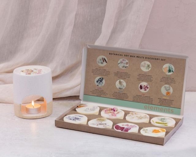 Boxed gift set of wax melts next to a wax melt holder with a lit candle