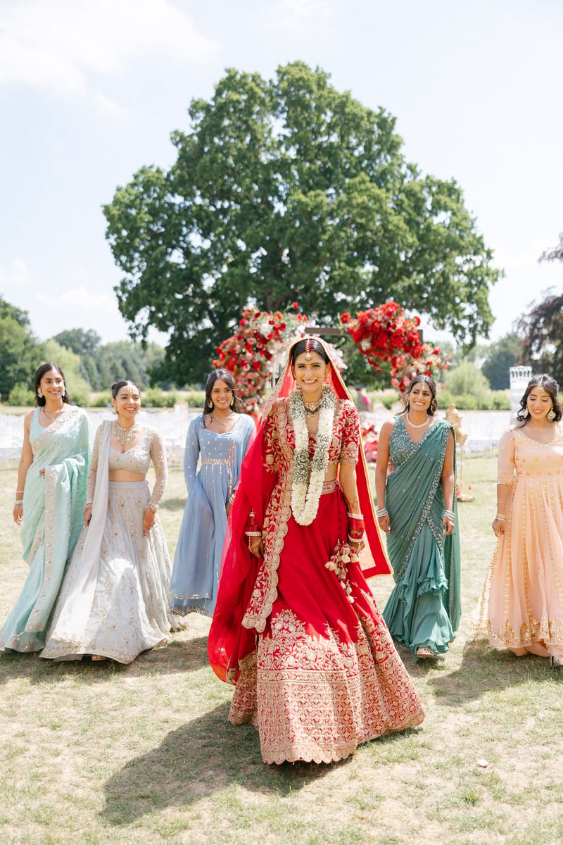 a Hindu bride in traditional red dress walking with her female wedding party also in traditional Indian dress