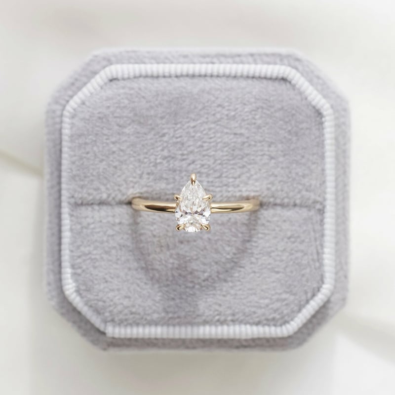 a pear-cut diamond ring on a yellow gold band tucked inside a grey cushioned ring box