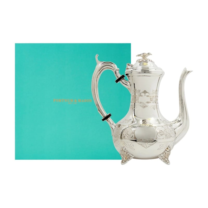 A silver engraved coffee pot next to a fortnum and mason gift box