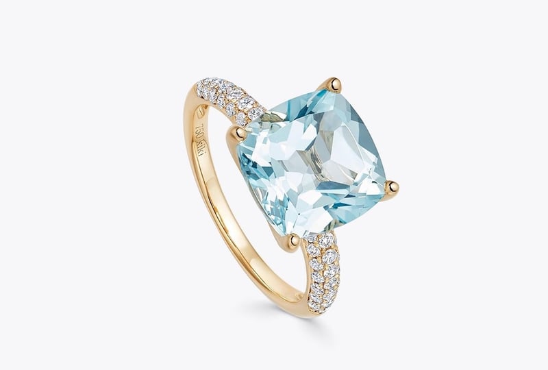 a yellow gold engagement ring with cushion-cut blue topaz stone and smaller diamonds on the band