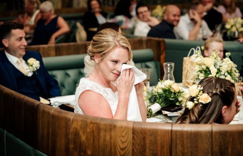 a bride wiping tears from her eyes and smiling during the wedding speeches