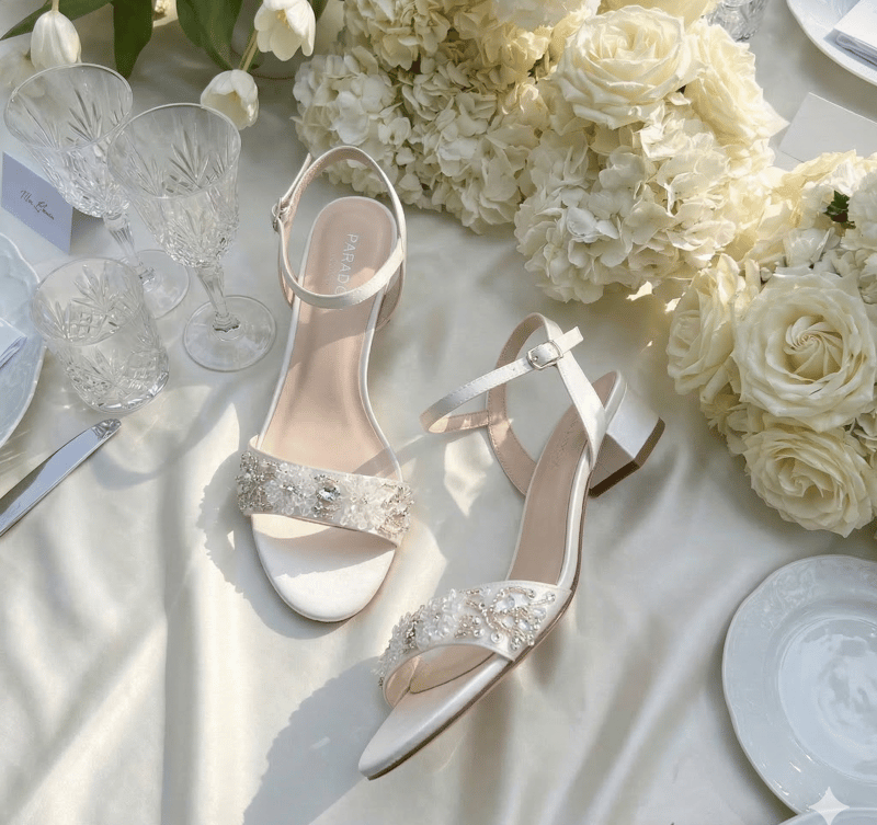 a pair of pearl and bead embellished flat sandals on a wedding table with flowers and glassware