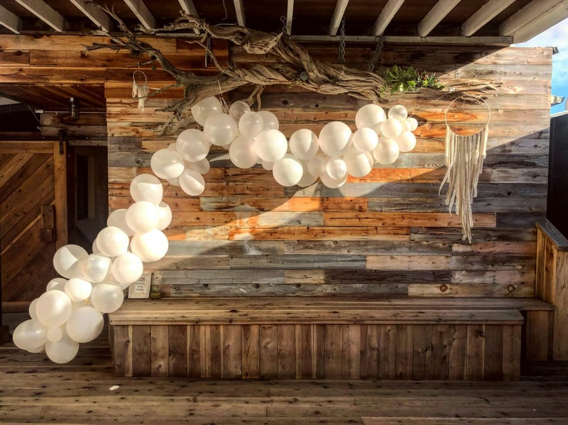 a cluster of white balloons arranged into an arch against a wooden wall