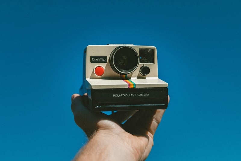 outstretched hand holding a vintage polaroid camera