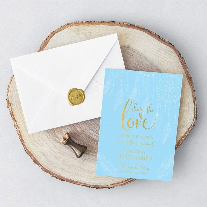 a blue and gold wedding invitation with white envelope and wax seal on a log slice