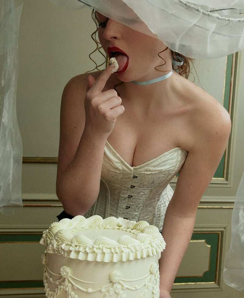 Bride eating icing from a wedding cake styled to suit the messy coquette wedding trend