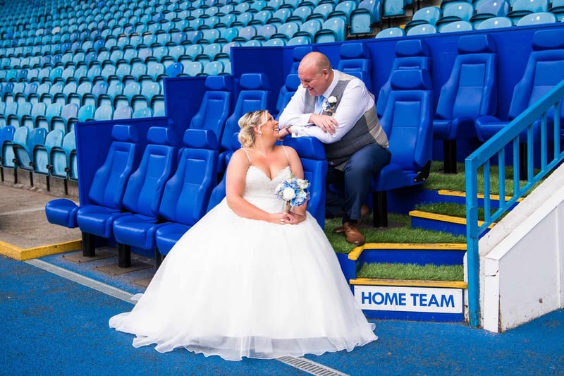 A bride and groom sitting in the blue stadium seats at Hillsborough, Sheffield Wednesday's ground, next to a HOME TEAM sign