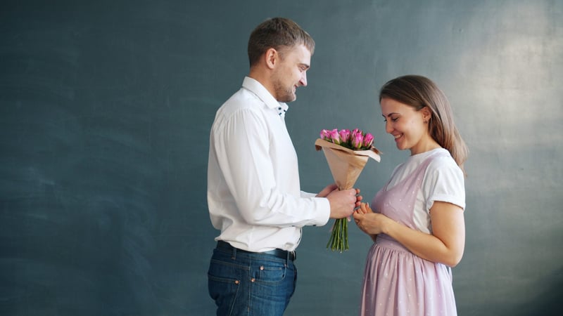 Man giving a bunch of pink tulips wrapped in brown paper to a woman in a pink dress