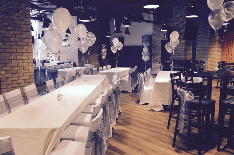A wedding reception room at Molineux Stadium, Wolverhampton, with long banquet tables, white linens and silver balloon decorations