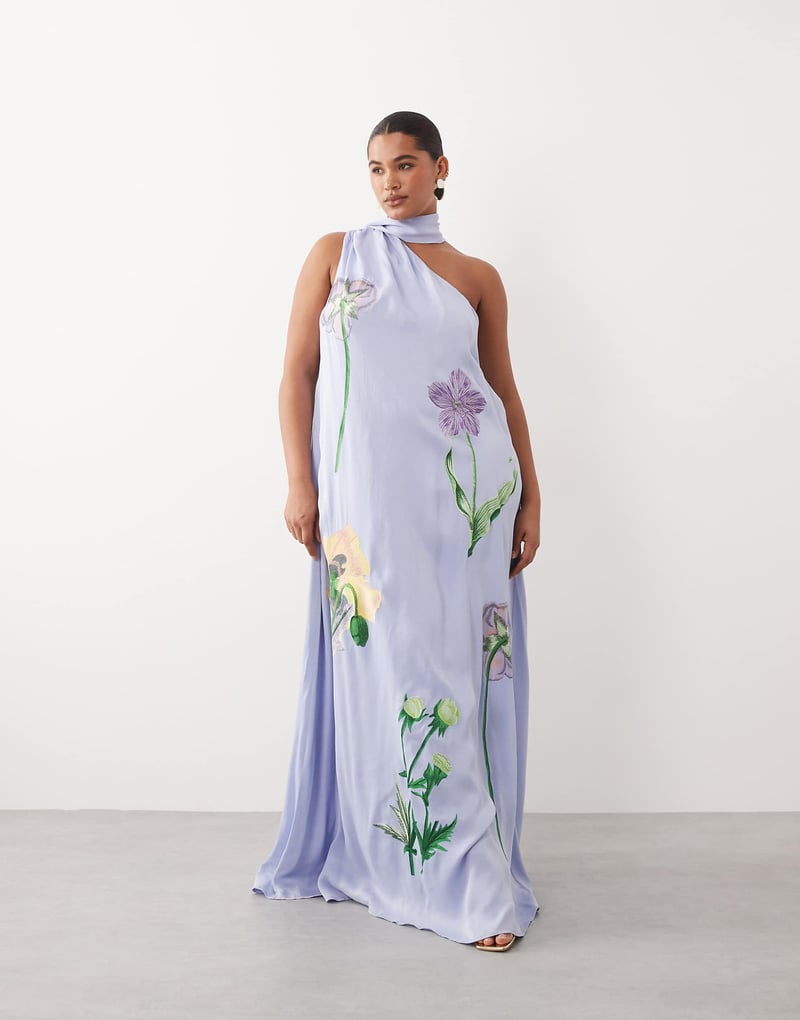 plus size model wears a one-shoulder maxi dress in dusky blue with embroidered floral detail.