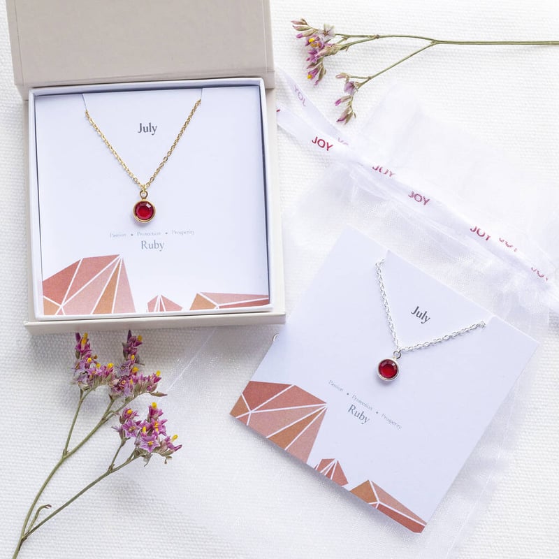 two ruby necklaces on gold chains in white boxes on a white surface