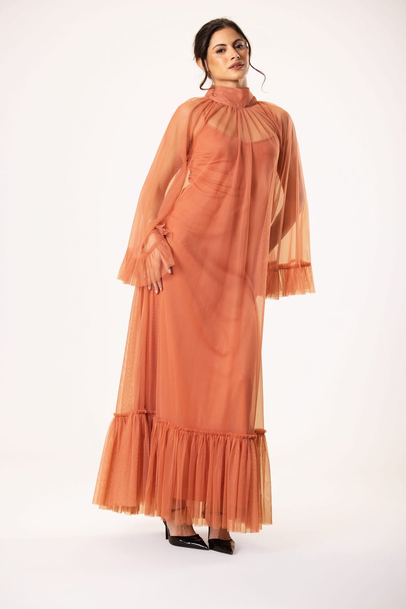 a plus size model wears a terracotta coloured maxi dress with sheer chiffon overlay