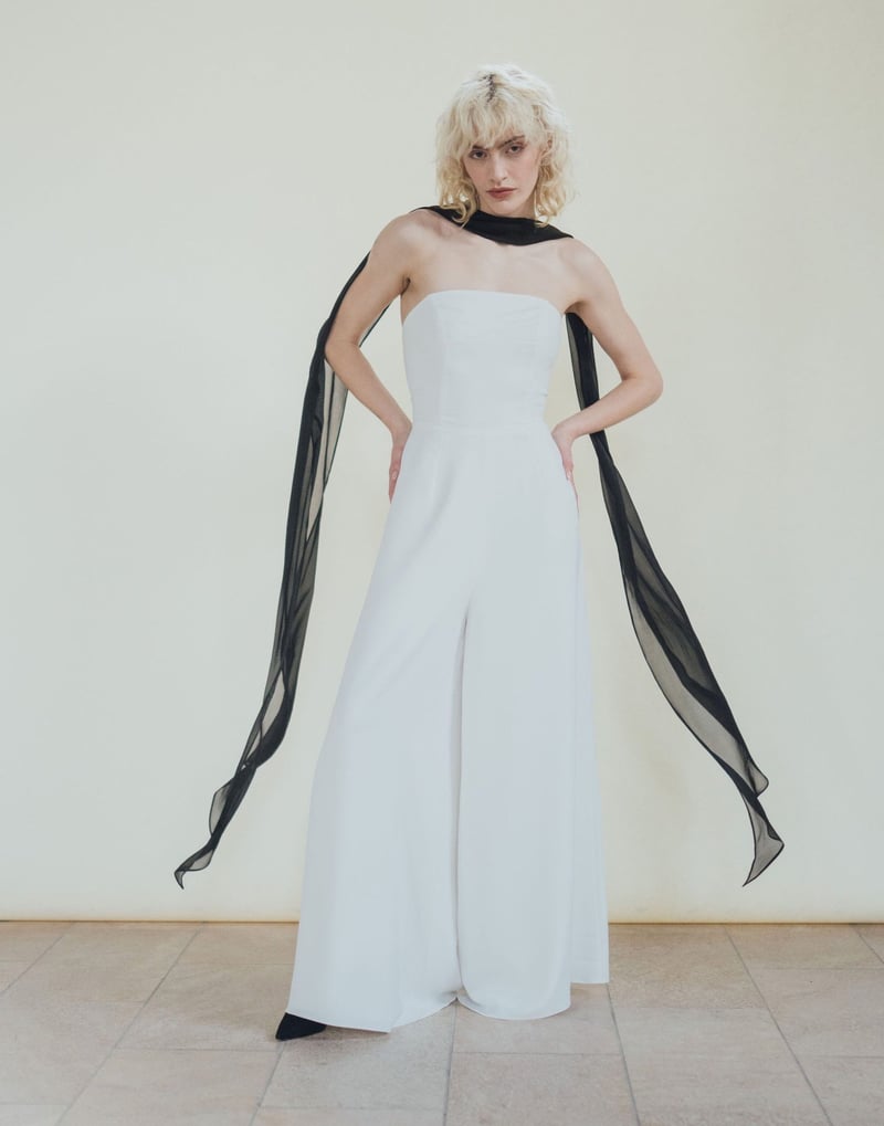 a model wears a strapless white wide-leg jumpsuit with a black scarf.