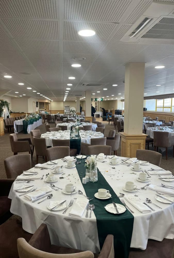 A wedding reception room at Notts County Football Club with round tables set with white linens and dark green table runners