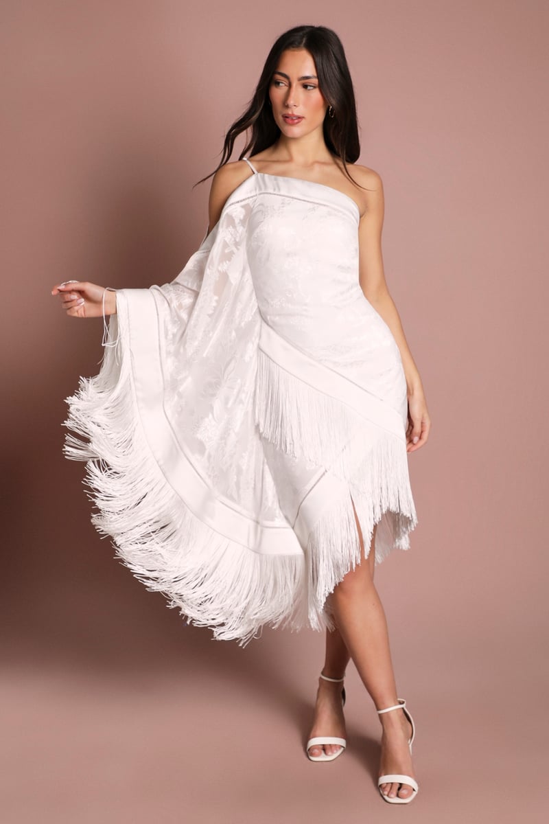 a model wears a knee length wedding dress with asymmetric hem and fringing.