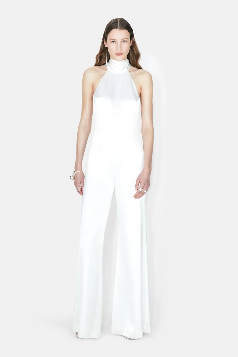 a model wears a silk-satin wide-leg jumpsuit with tie-sash halterneck.