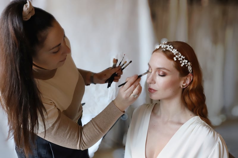 a red-headed bride is having her eye makeup applied by a wedding makeup artist.