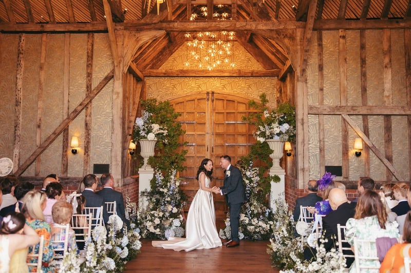 a bride and groom laugh during their ceremony in a barn wedding venue as guests look on.