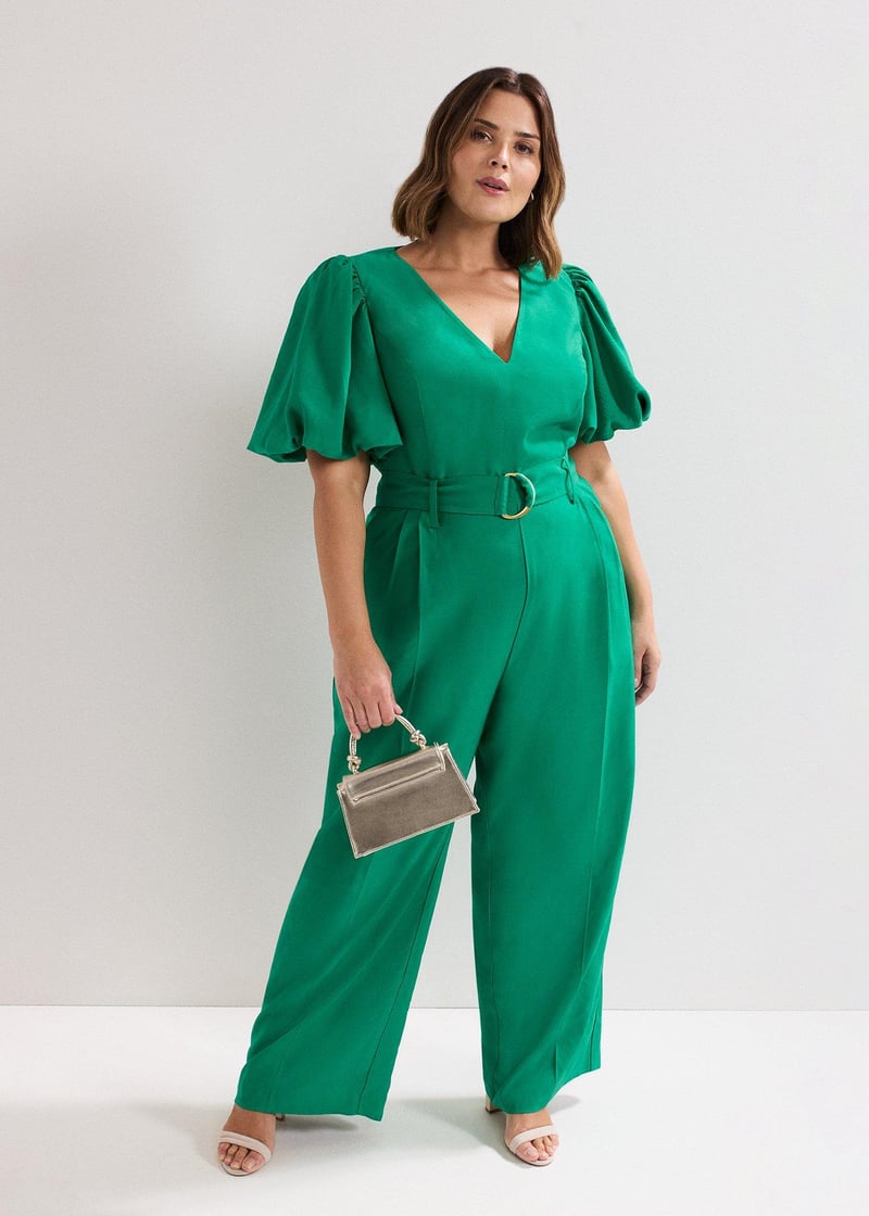 a curve model wears a wedding guest jumpsuit in green with short puff sleeves and v neckline.