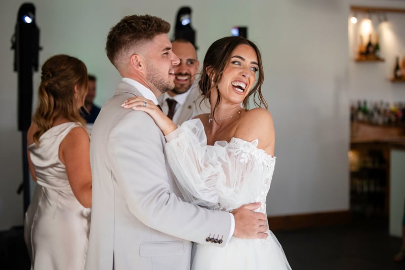 a bride and groom smile as they look over at their guests while dancing.