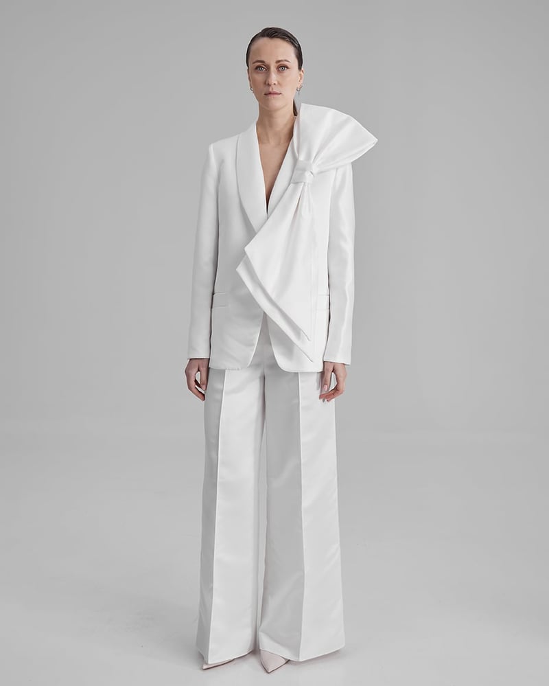 a model wears a white wedding suit with oversized bow corsage on the lapel of the jacket.