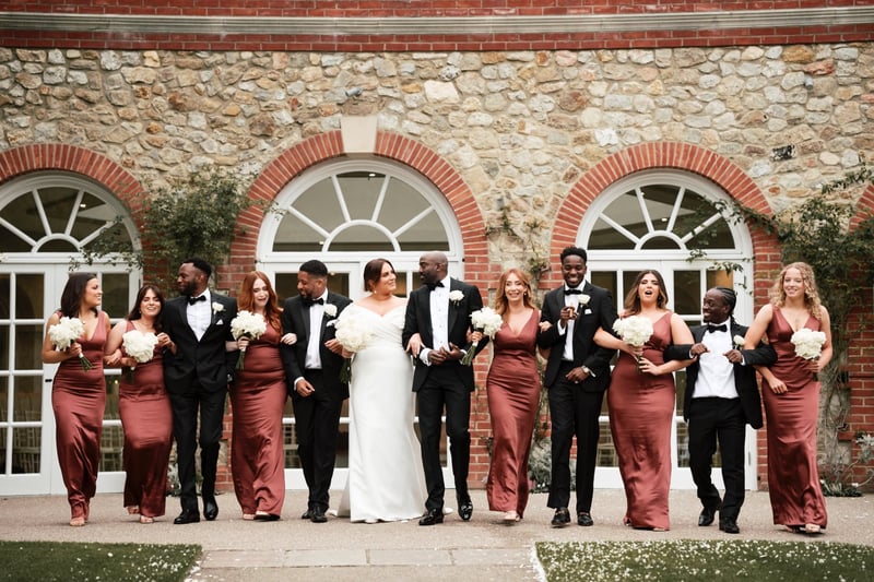 a wedding party walk arm in arm in front of a wedding venue.