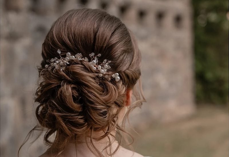 Rückansicht einer Braut mit romantischer Hochsteckfrisur, lockerem Dutt und funkelndem Haarschmuck bei einer Hochzeit im Freien.