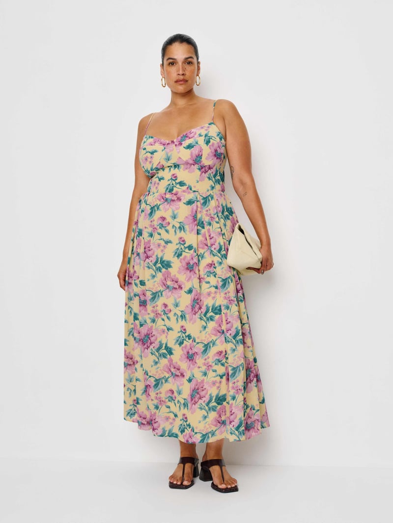 a plus size model wears a floral print midi strappy summer dress with cream clutch bag.