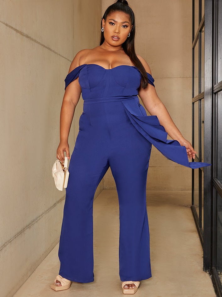 a curve model wears a blue fitted jumpsuit with bardot-style neckline.
