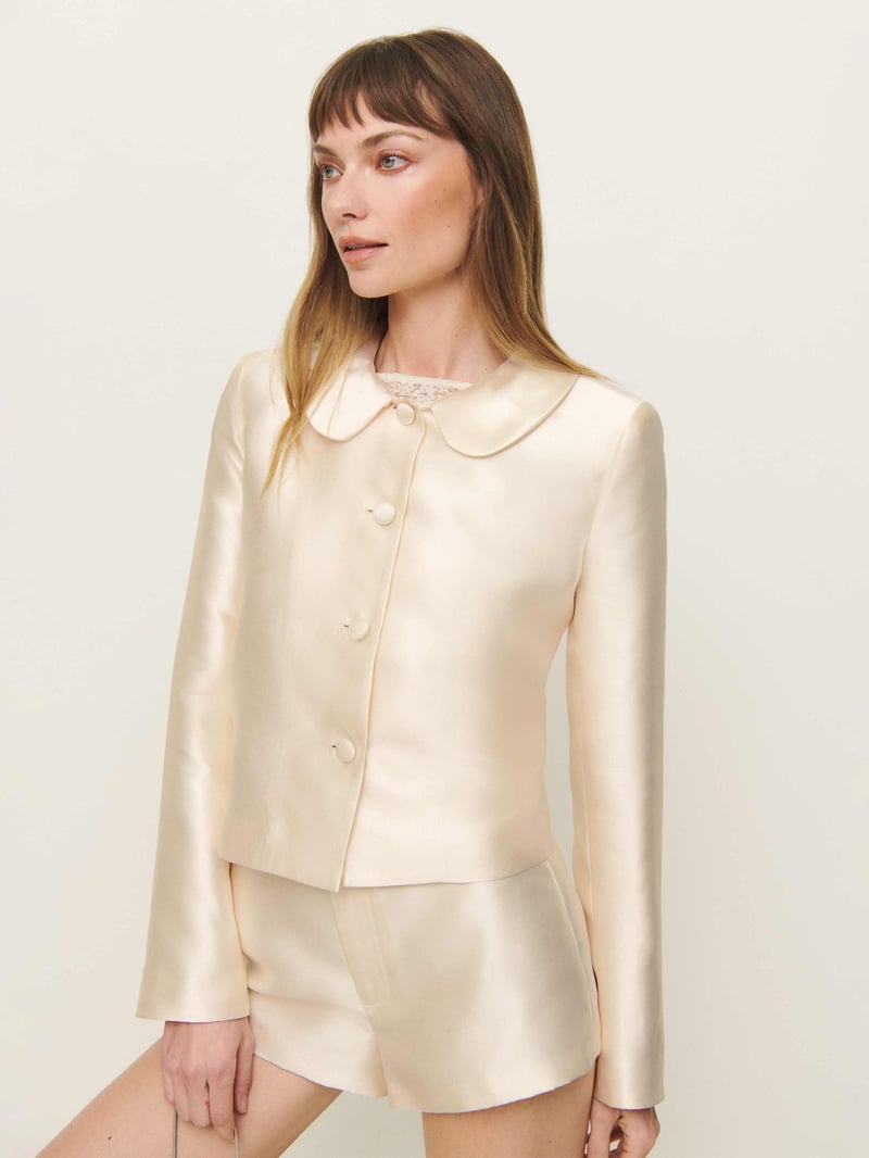 a model wears a cream bridal suit featuring high-rise shorts and a collared jacket.