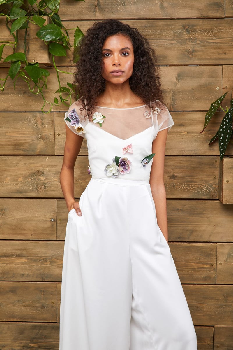 a model wears a strappy wide leg jumpsuit with sheer chiffon overlay embellished with colourful 3D flowers.