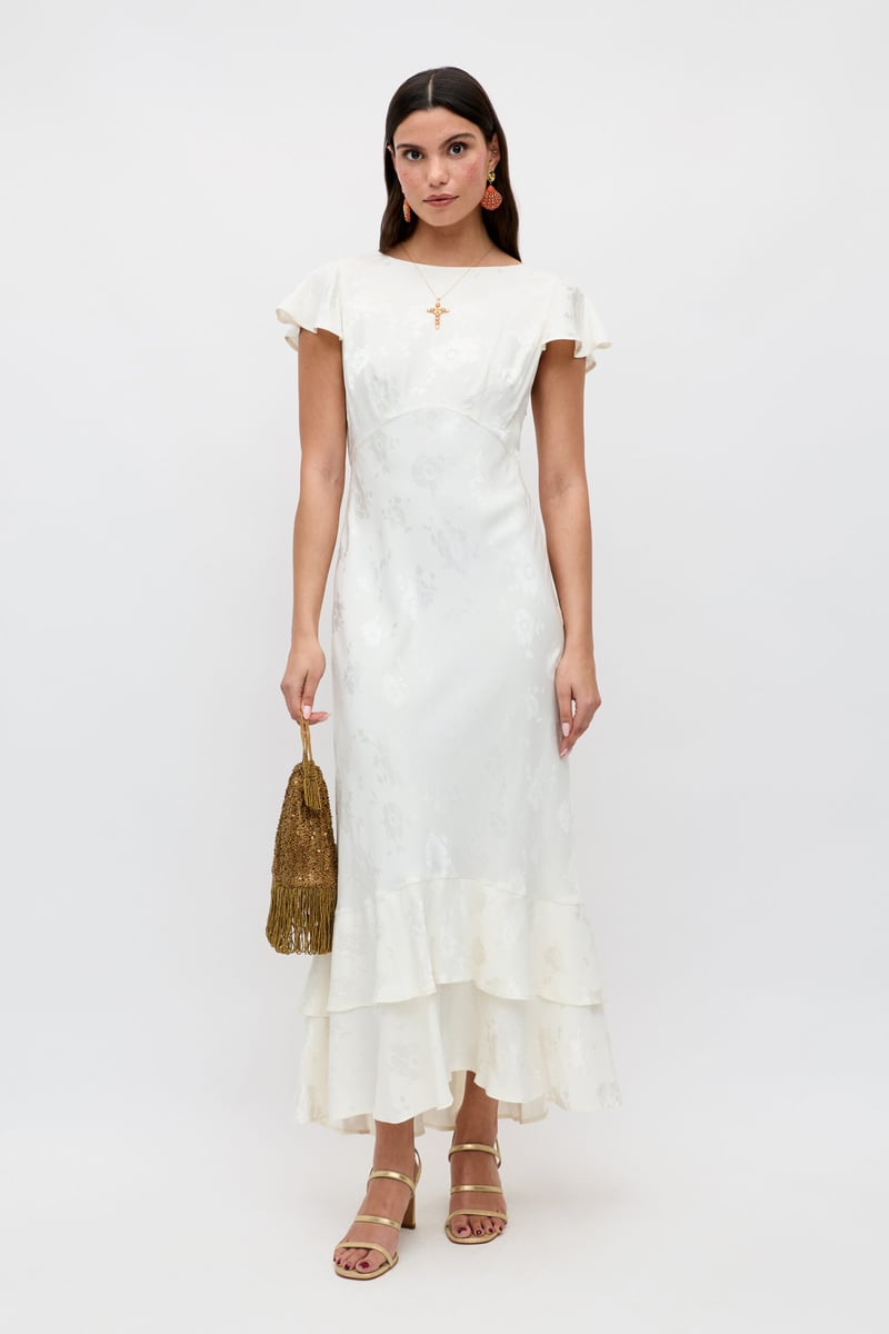 a model wears a jaquard satin fabric ankle length wedding dress with short flutter sleeves and tiered skirt.