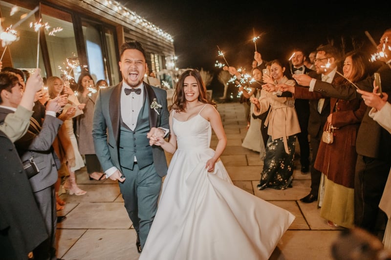 a bride and groom walk through a tunnel of sparklers to their wedding reception.