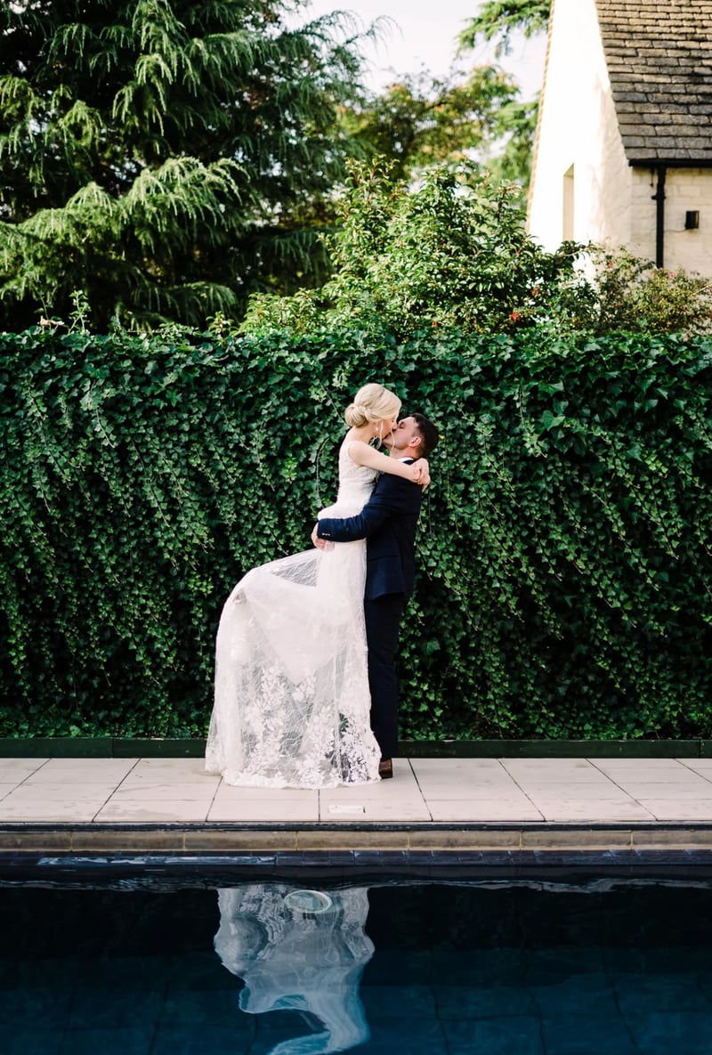 Bride and groom kissing at Ellenborough Park, Gloucestershire's only AA Five Star hotel and wedding venue, with outdoor heated pool at 30°C