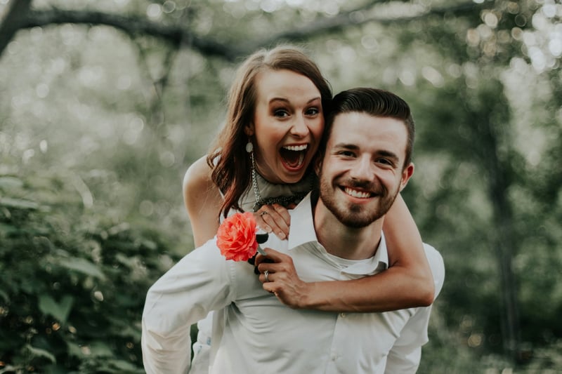 Couple embracing in a wild garden, the woman holding an orange flower clinging to the man's back and smiling