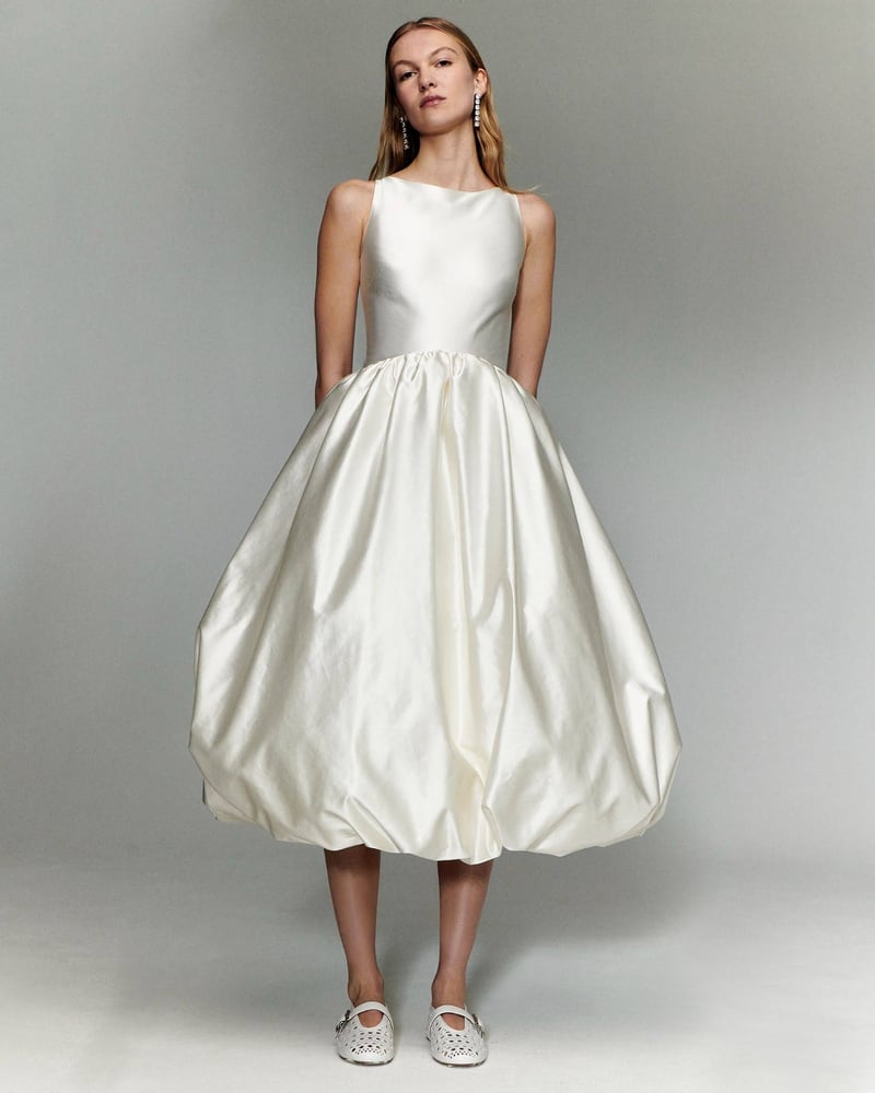 a model wears an off white satin sleeveless midi wedding dress with bubble hem.