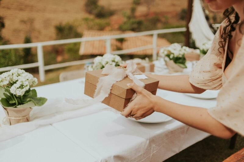Person hält dekorierte Geschenkbox bei einer Hochzeit im Freien über einem festlich gedeckten Tisch