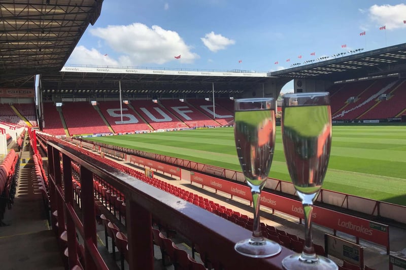 Two champagne flutes on the edge of the stands at Bramall Lane stadium, with the SUFC letters and football pitch in the background
