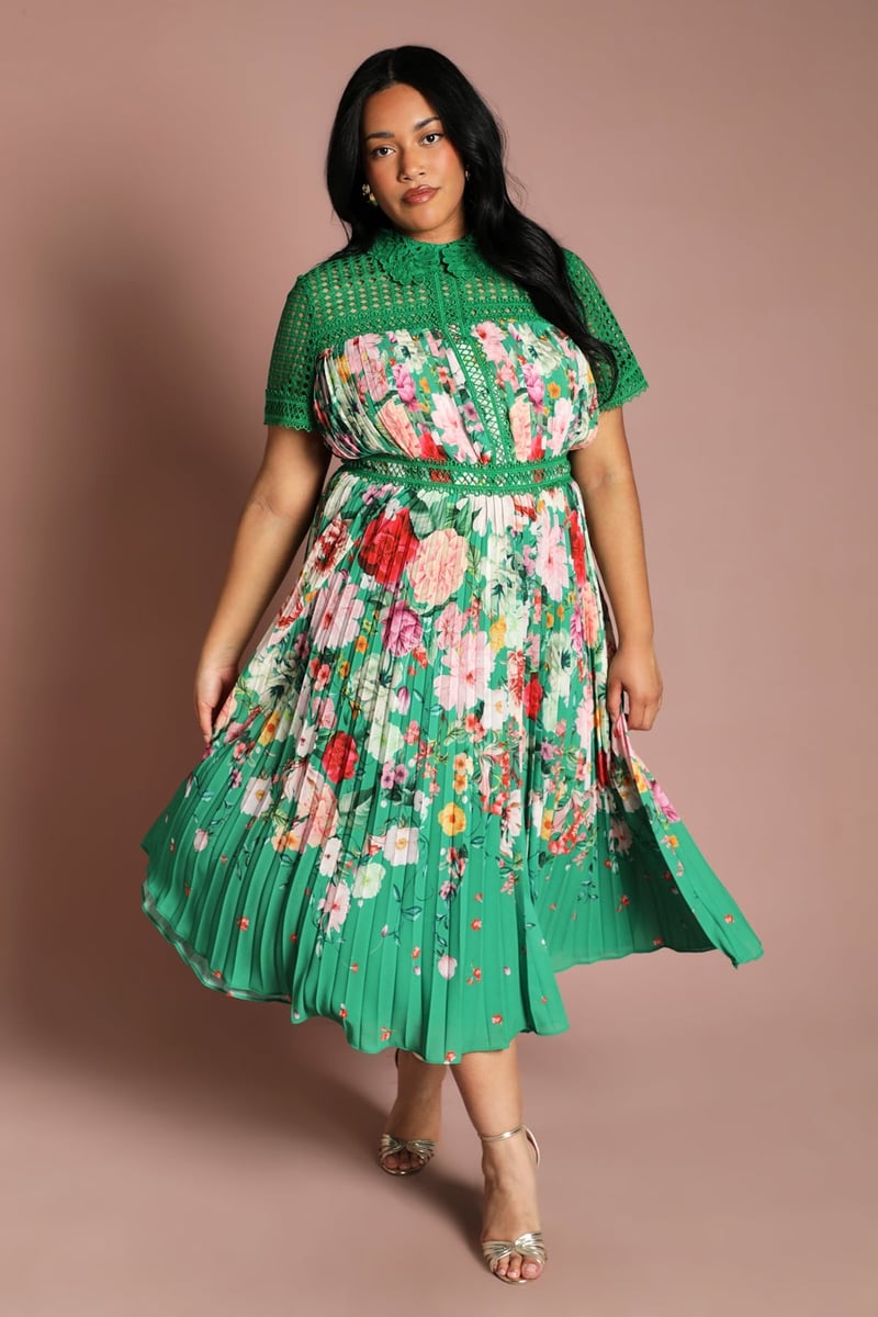 a plus size model wears a green midi dress with colourful floral print and crochet-style detail on the neckline.