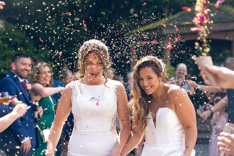 two brides hold hands as they walk through a shower of confetti.