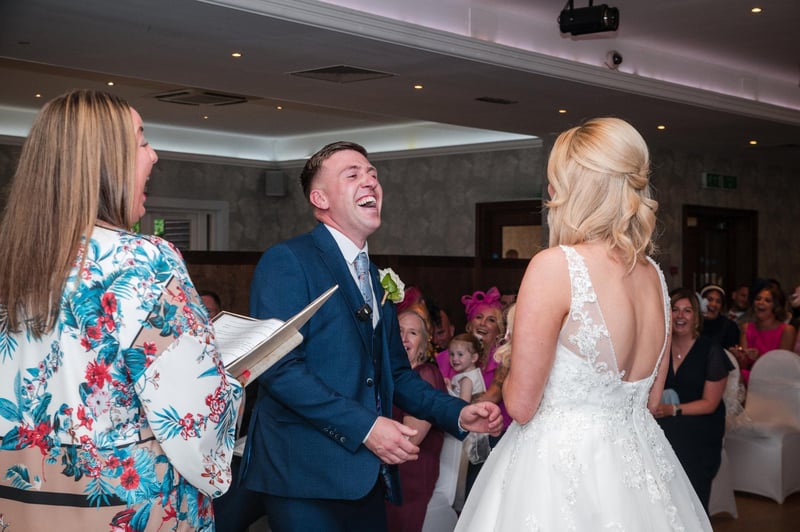 a groom laughs during the wedding ceremony as he holds hands with his bride.