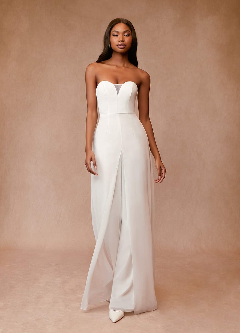 a model wears a white wedding jumpsuit with sweetheart neckline and chiffon overlay to make it look like a dress.