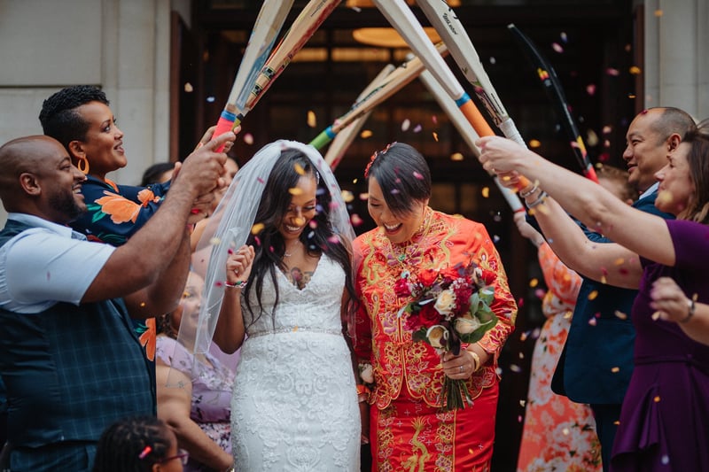 two brides, one wearing red, leave their wedding ceremony as guests throw confetti