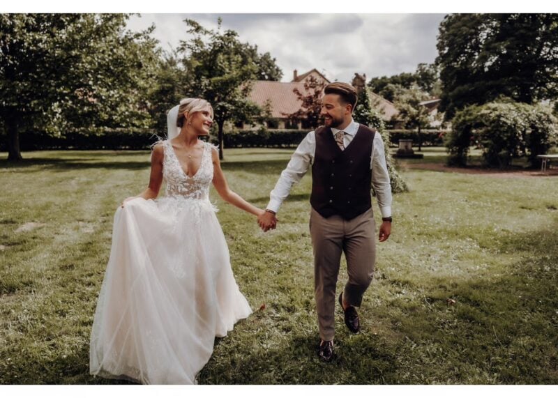 Brautpaar läuft Hand in Hand über eine Wiese bei einer romantischen Outdoor-Hochzeit