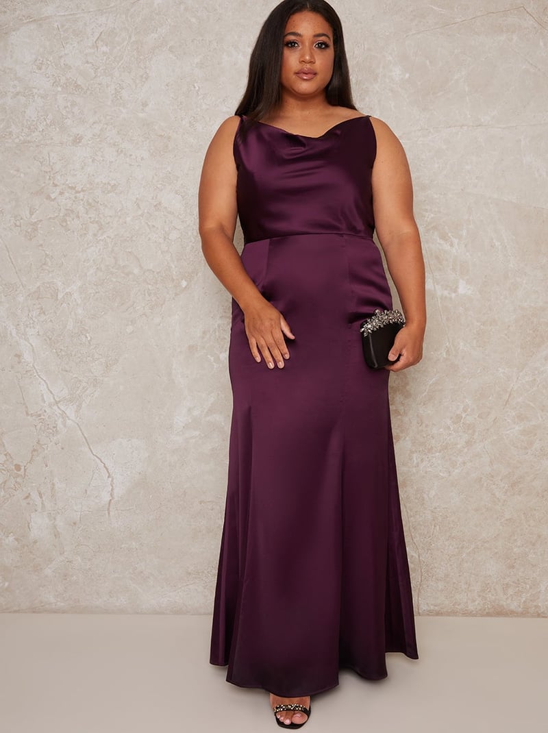 a plus size model wears a plum-coloured satin wedding guest maxi dress with cowl neck.