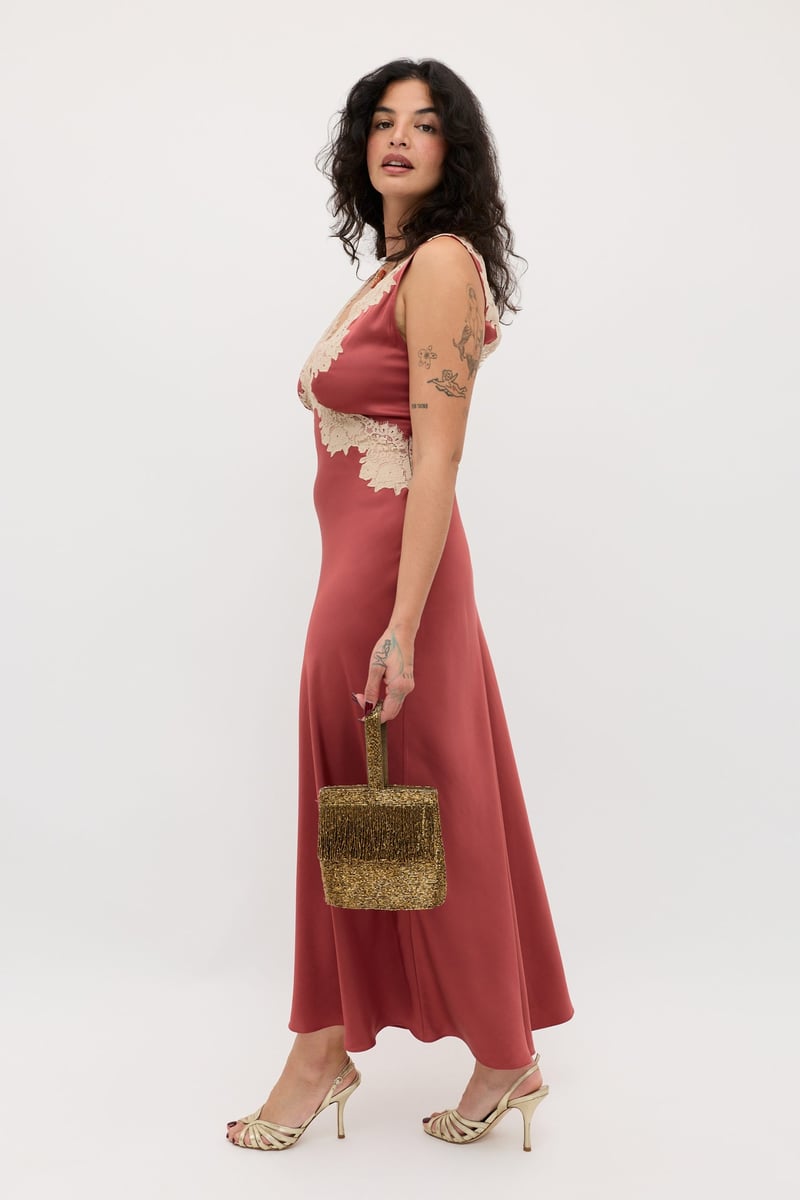 a curve model wears a rose-coloured satin slip midi dress with lace detail around the bodice.
