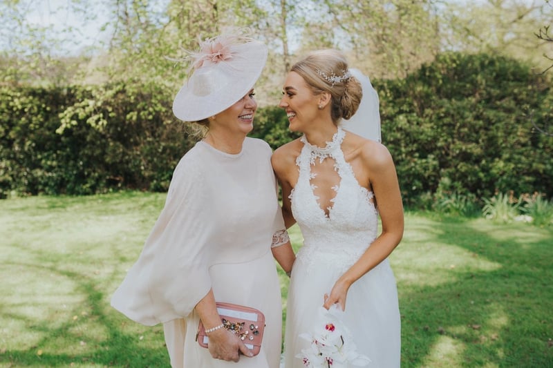 a bride and her mum smile at each other, both are wearing their wedding attire.