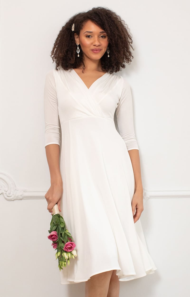 a model wears a knee length wedding dress with chiffon three-quarter-length sleeves and holds a bouquet